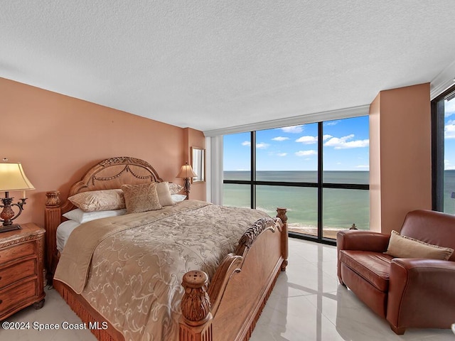 bedroom with access to outside, a textured ceiling, a water view, and multiple windows