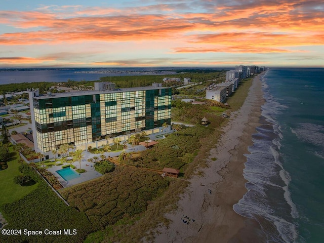 aerial view at dusk featuring a view of the beach and a water view