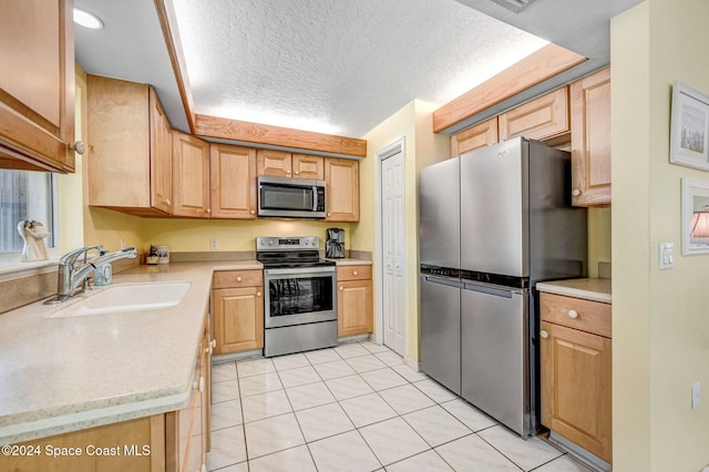 kitchen with sink, a textured ceiling, light brown cabinetry, appliances with stainless steel finishes, and light tile patterned flooring