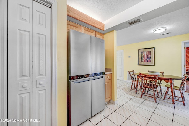 kitchen with stainless steel refrigerator, light brown cabinetry, light tile patterned flooring, and a textured ceiling