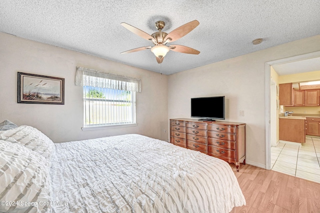 bedroom with connected bathroom, ceiling fan, light hardwood / wood-style floors, and a textured ceiling