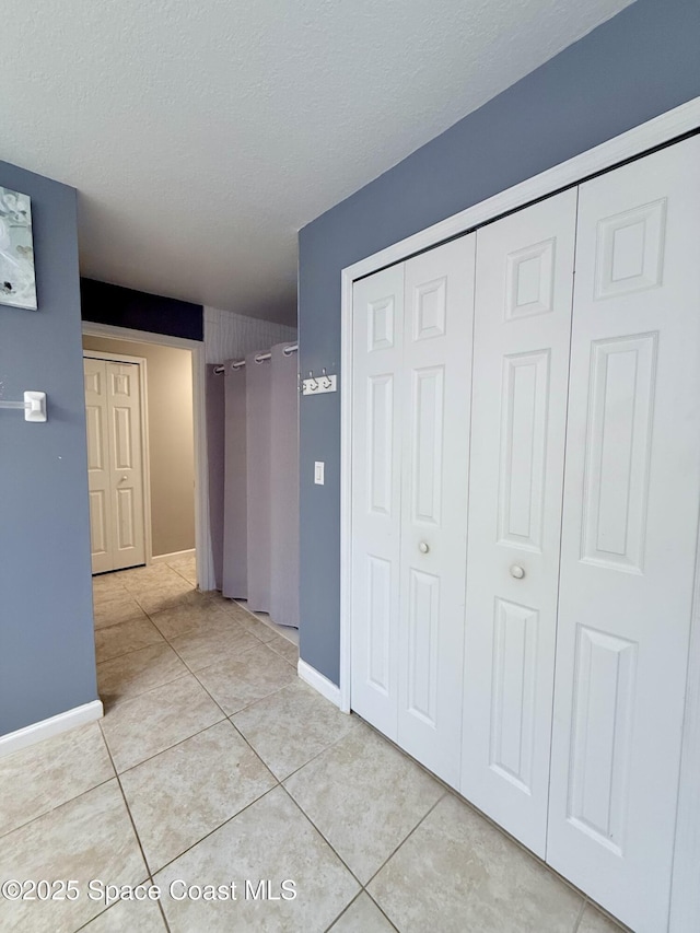 hall with a textured ceiling, baseboards, and light tile patterned floors