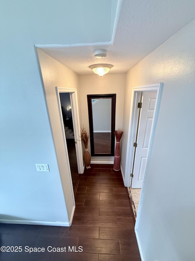 hallway with wood finish floors, a textured ceiling, and baseboards