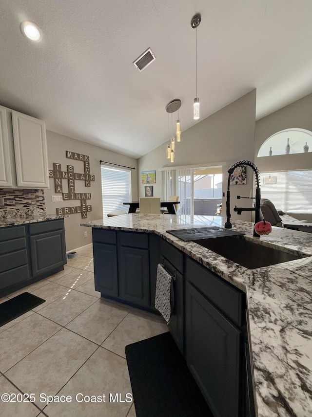 kitchen with light stone counters, light tile patterned floors, visible vents, vaulted ceiling, and a sink