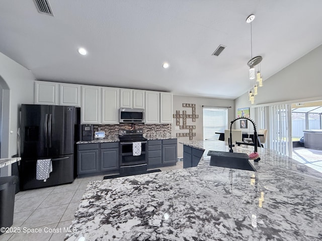 kitchen with stainless steel microwave, electric range oven, freestanding refrigerator, a sink, and light stone countertops