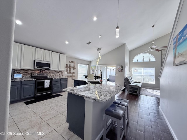 kitchen with black / electric stove, light stone counters, a sink, decorative backsplash, and stainless steel microwave