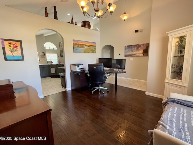 office featuring arched walkways, a chandelier, a high ceiling, wood finished floors, and baseboards