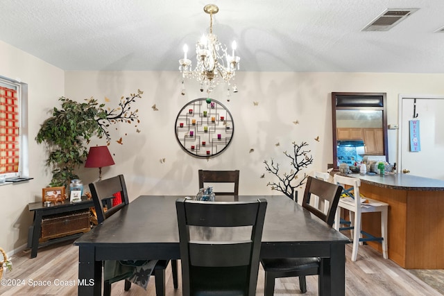 dining space featuring light hardwood / wood-style floors, a textured ceiling, and an inviting chandelier