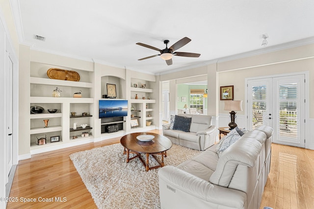 living room featuring built in shelves, french doors, ceiling fan, light hardwood / wood-style flooring, and crown molding