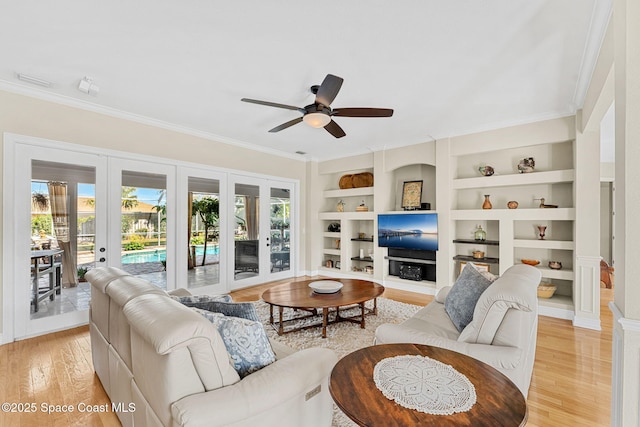 living room featuring built in shelves, french doors, ceiling fan, light hardwood / wood-style flooring, and crown molding