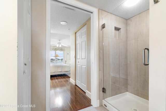 bathroom with a shower with shower door, ceiling fan, wood-type flooring, and a textured ceiling