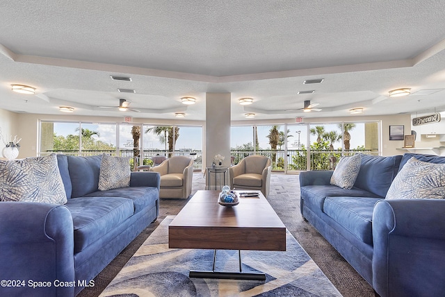 living room featuring dark colored carpet, a textured ceiling, a raised ceiling, and ceiling fan