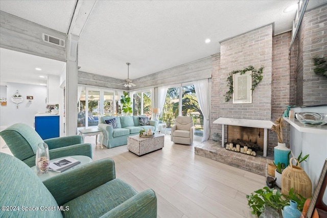 living room with a fireplace, a textured ceiling, light hardwood / wood-style flooring, and ceiling fan