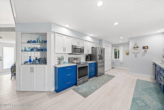 kitchen with blue cabinets, appliances with stainless steel finishes, tasteful backsplash, light hardwood / wood-style floors, and white cabinetry