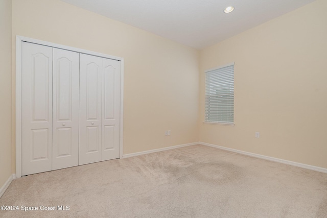 unfurnished bedroom with light colored carpet and a closet