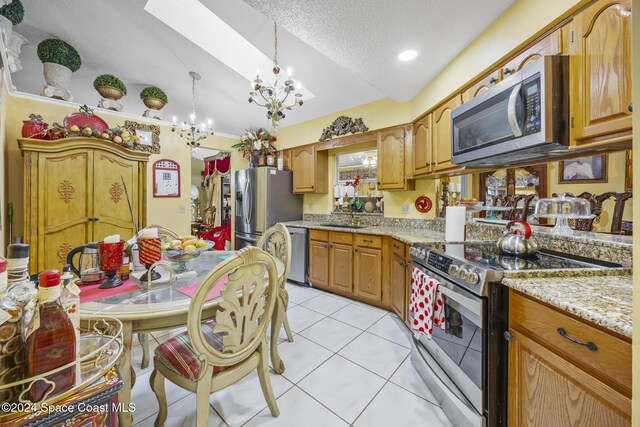 kitchen featuring light stone countertops, sink, stainless steel appliances, a notable chandelier, and light tile patterned floors