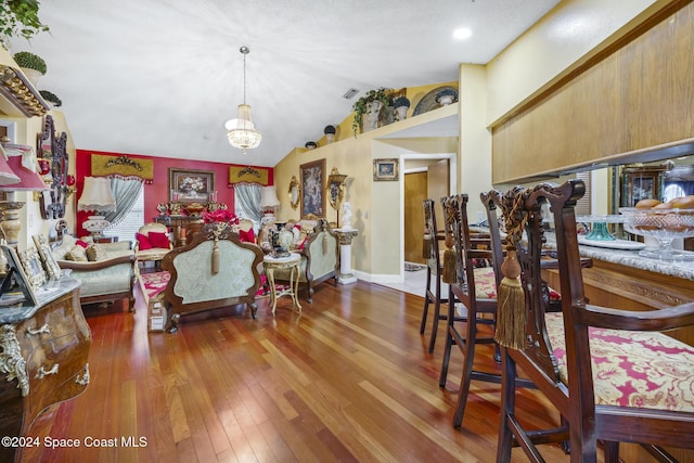 dining space with hardwood / wood-style floors, lofted ceiling, and an inviting chandelier