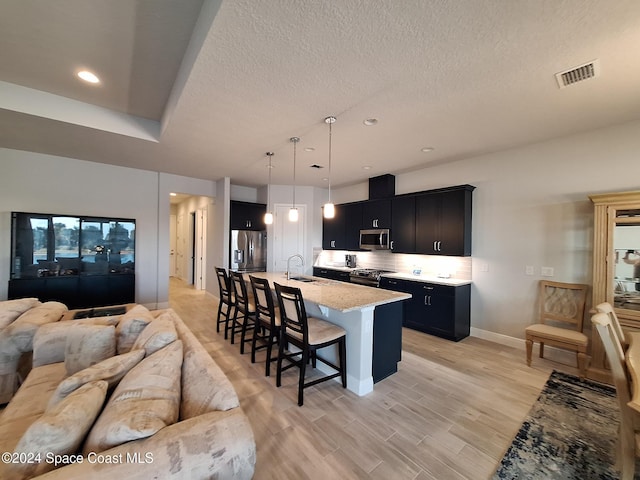 kitchen featuring decorative light fixtures, a kitchen bar, a center island with sink, appliances with stainless steel finishes, and light wood-type flooring