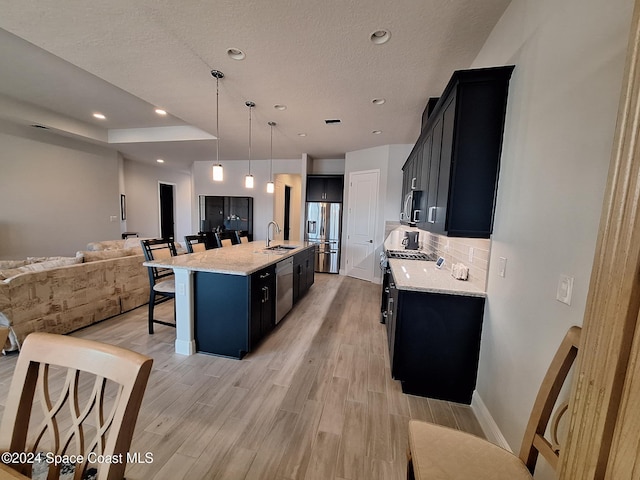 kitchen with sink, hanging light fixtures, stainless steel appliances, a kitchen breakfast bar, and a kitchen island with sink