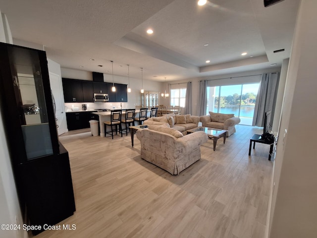 living room featuring a tray ceiling, a water view, and light hardwood / wood-style floors