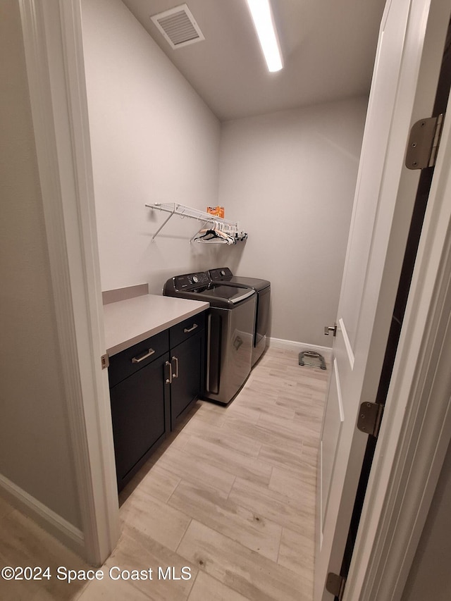 clothes washing area featuring cabinets, separate washer and dryer, and light wood-type flooring