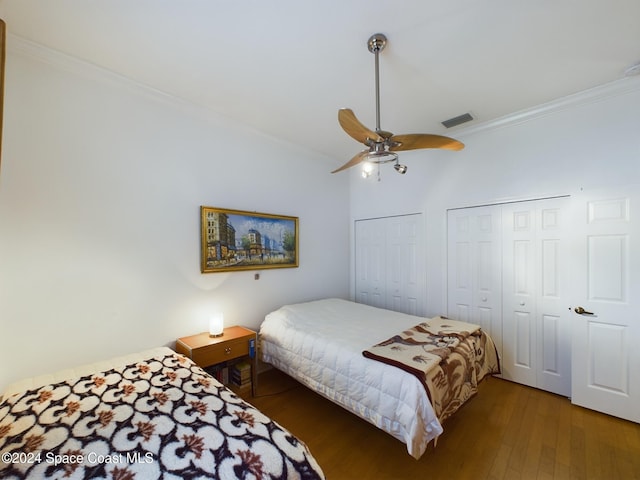 bedroom featuring multiple closets, dark hardwood / wood-style floors, ceiling fan, and crown molding