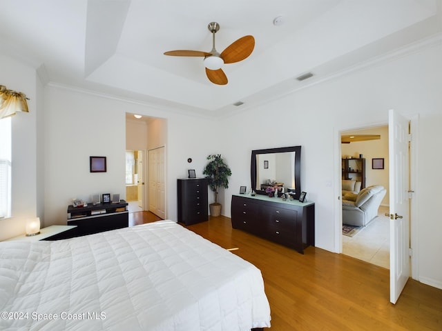 bedroom featuring ceiling fan, wood-type flooring, crown molding, and a tray ceiling