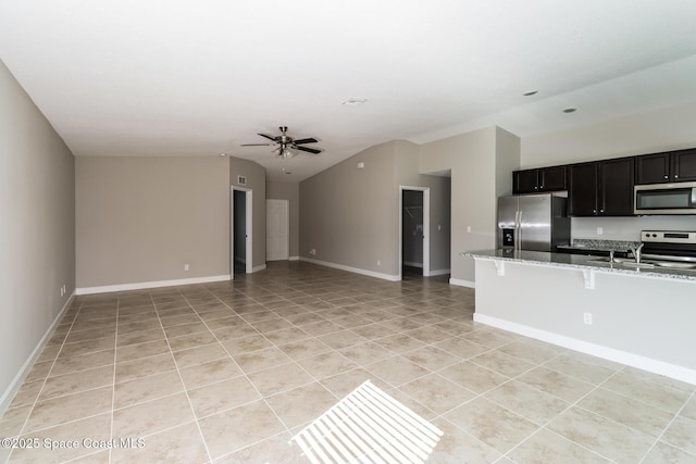 kitchen featuring lofted ceiling, stainless steel appliances, a kitchen breakfast bar, light stone counters, and light tile patterned flooring