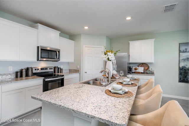 kitchen featuring stainless steel appliances, a kitchen island with sink, white cabinetry, and sink