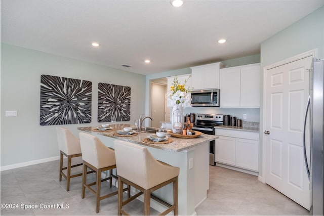 kitchen with a breakfast bar area, appliances with stainless steel finishes, an island with sink, light stone counters, and white cabinetry