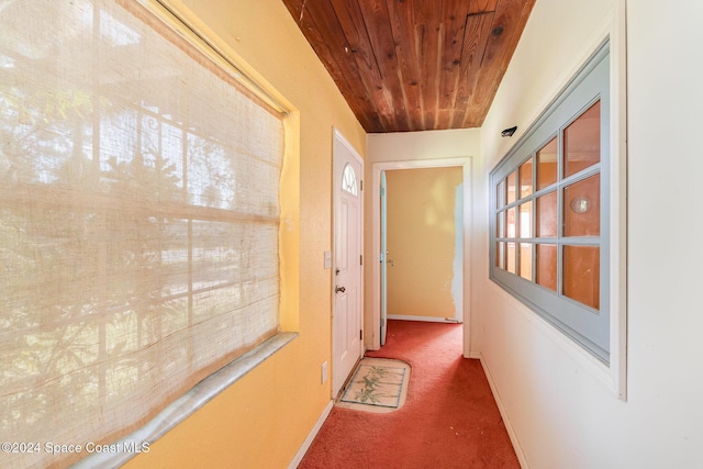 hallway featuring dark colored carpet and wooden ceiling