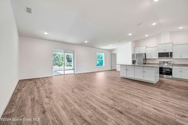 kitchen with stainless steel appliances, a center island with sink, light hardwood / wood-style flooring, white cabinets, and lofted ceiling