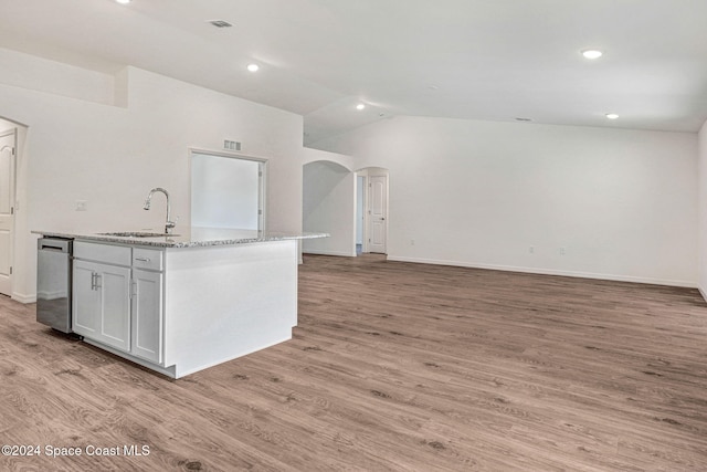 kitchen featuring light stone countertops, light wood-type flooring, vaulted ceiling, a kitchen island with sink, and sink