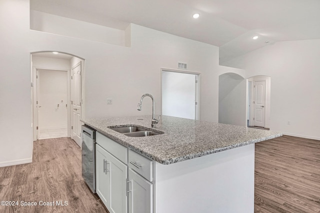 kitchen featuring a kitchen island with sink, sink, stainless steel dishwasher, light wood-type flooring, and light stone countertops