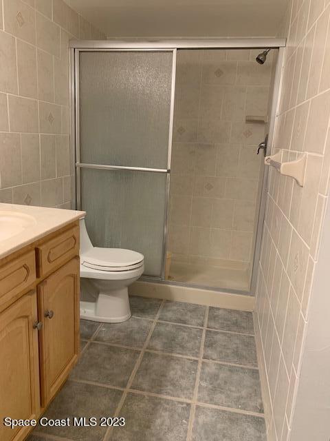 bathroom featuring vanity, tile walls, tile patterned flooring, toilet, and a shower with shower door