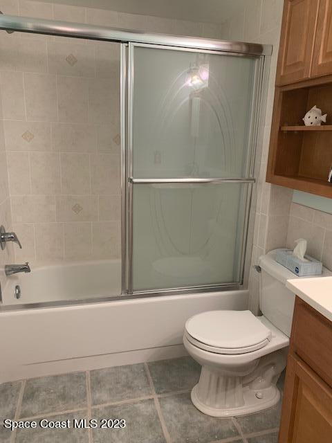 full bathroom with combined bath / shower with glass door, tile patterned floors, vanity, and toilet