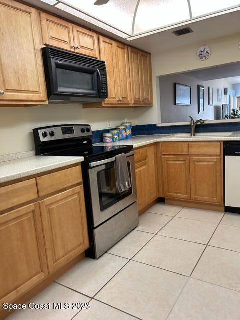 kitchen with dishwasher, light tile patterned floors, stainless steel range with electric cooktop, and sink