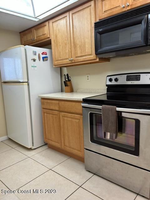 kitchen featuring light tile patterned floors, white fridge, and electric stove