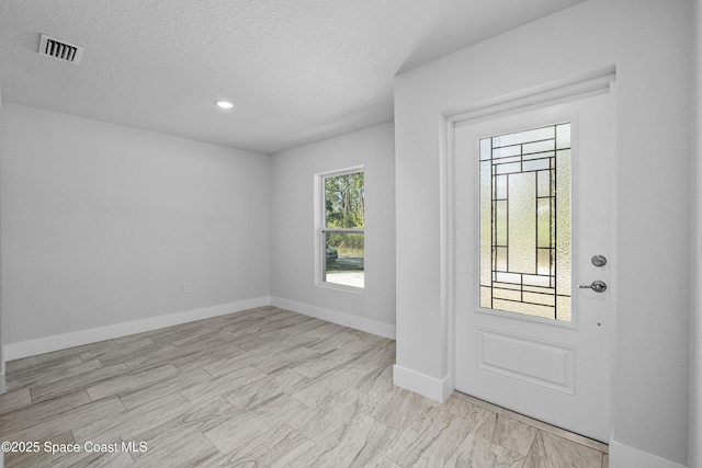 foyer entrance featuring baseboards, visible vents, and a textured ceiling