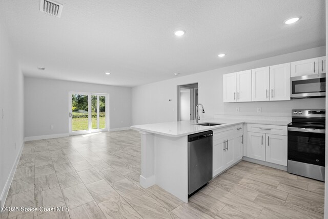 kitchen featuring appliances with stainless steel finishes, open floor plan, a peninsula, light countertops, and white cabinetry