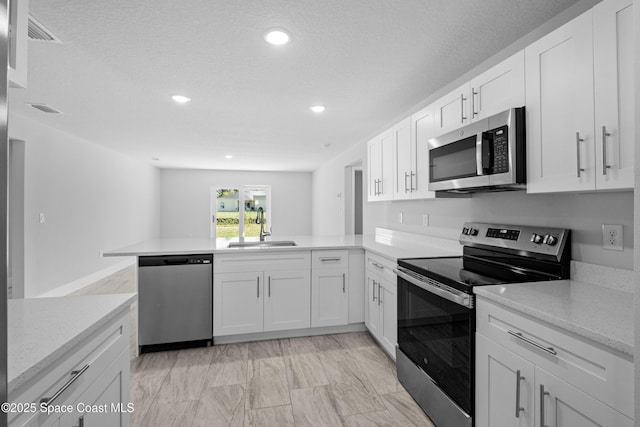 kitchen with visible vents, a peninsula, stainless steel appliances, white cabinetry, and a sink