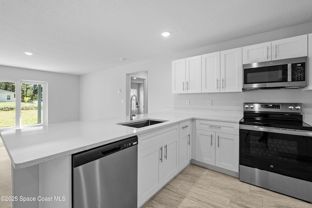 kitchen featuring appliances with stainless steel finishes, white cabinets, a sink, and a peninsula