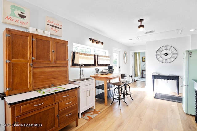 kitchen featuring sink, a textured ceiling, white fridge, and light hardwood / wood-style flooring