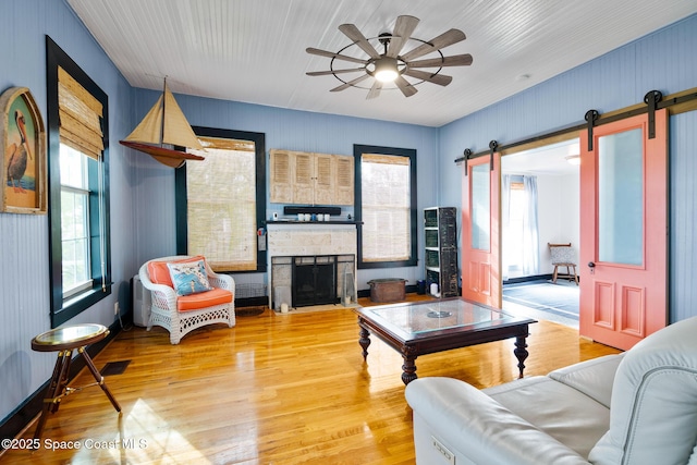 living room with ceiling fan, light hardwood / wood-style floors, and a stone fireplace