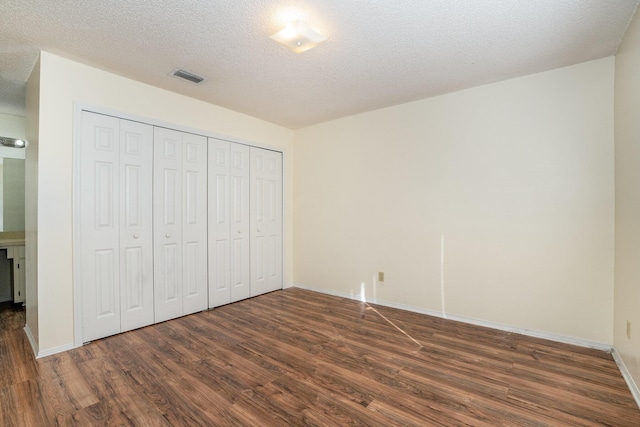 unfurnished bedroom featuring dark hardwood / wood-style floors, a textured ceiling, and a closet