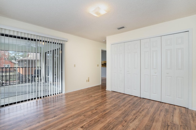 unfurnished bedroom with access to exterior, wood-type flooring, a textured ceiling, and a closet