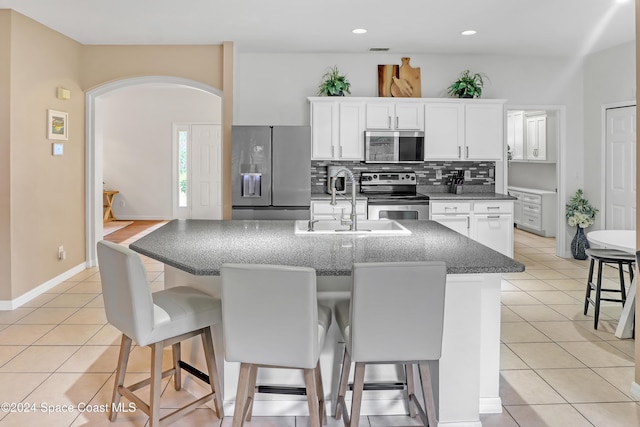 kitchen featuring a kitchen bar, stainless steel appliances, a kitchen island with sink, white cabinets, and light tile patterned flooring