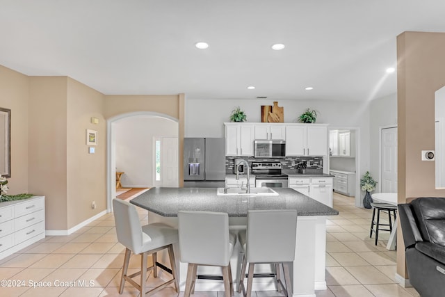 kitchen featuring decorative backsplash, appliances with stainless steel finishes, a kitchen island with sink, sink, and white cabinets