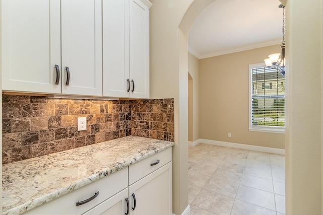 kitchen with light stone countertops, hanging light fixtures, backsplash, crown molding, and white cabinets