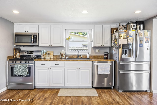 kitchen with sink, dark stone countertops, appliances with stainless steel finishes, dark hardwood / wood-style flooring, and white cabinetry